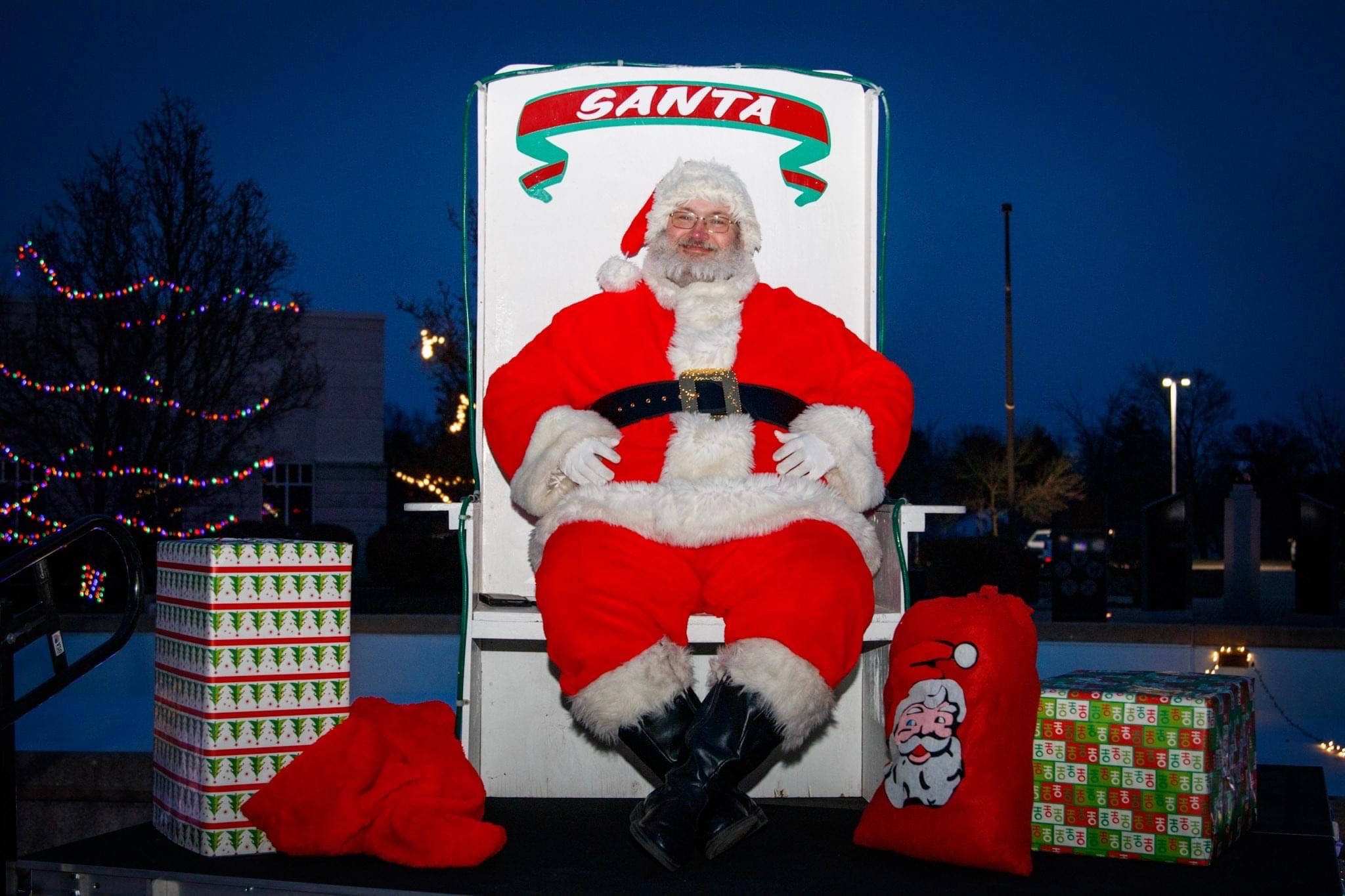 Santa Clause sitting on his chair on a stage outside at night.